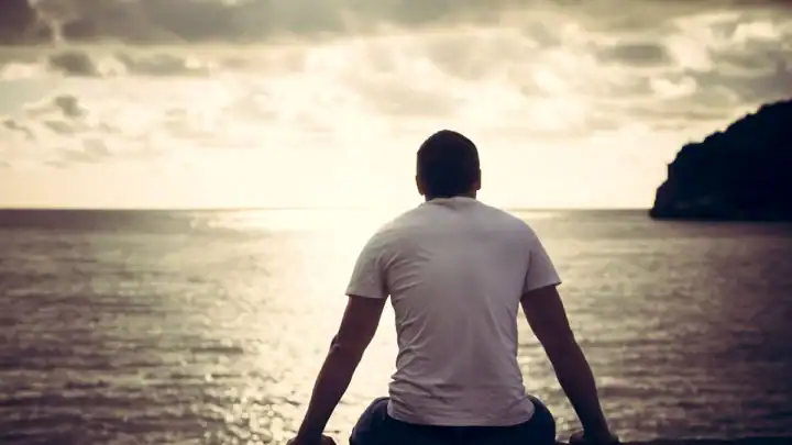 Man sitting and looking out at the ocean during sunset.