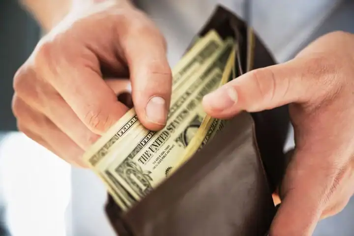 Person pulling U.S. dollar bills from a wallet.